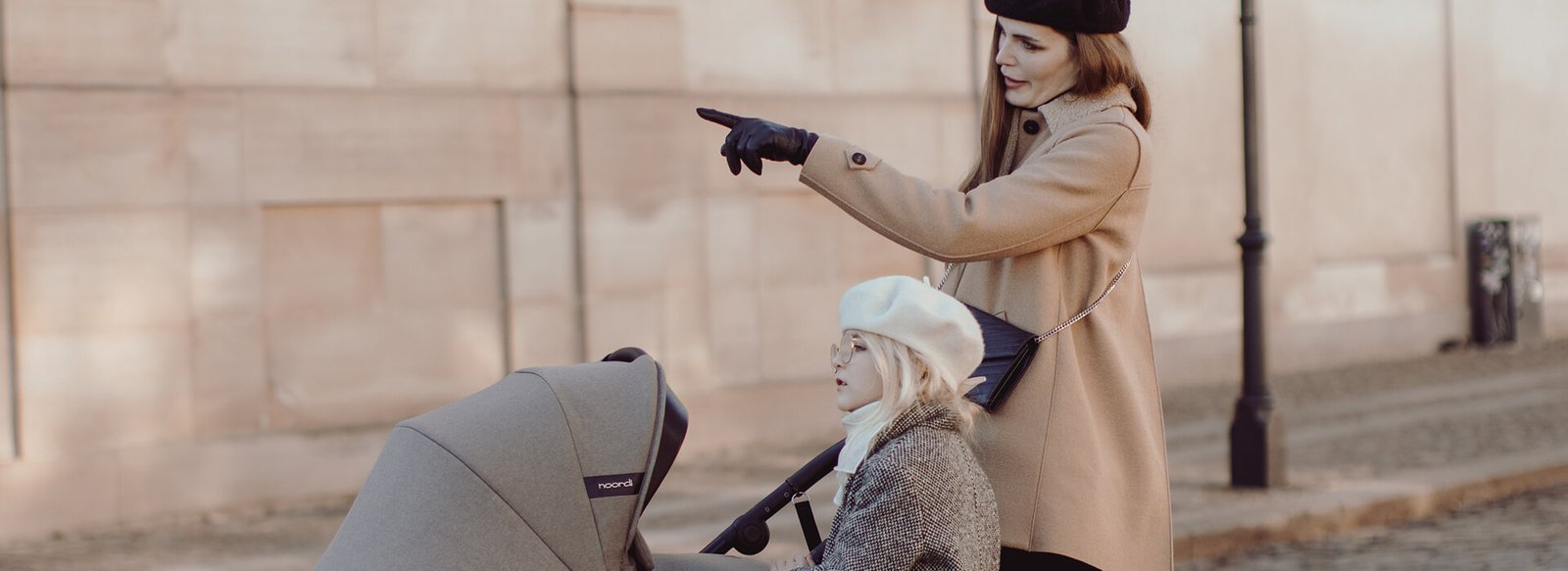 Mother pointing something out to her child sitting in a pram on an autumn city street