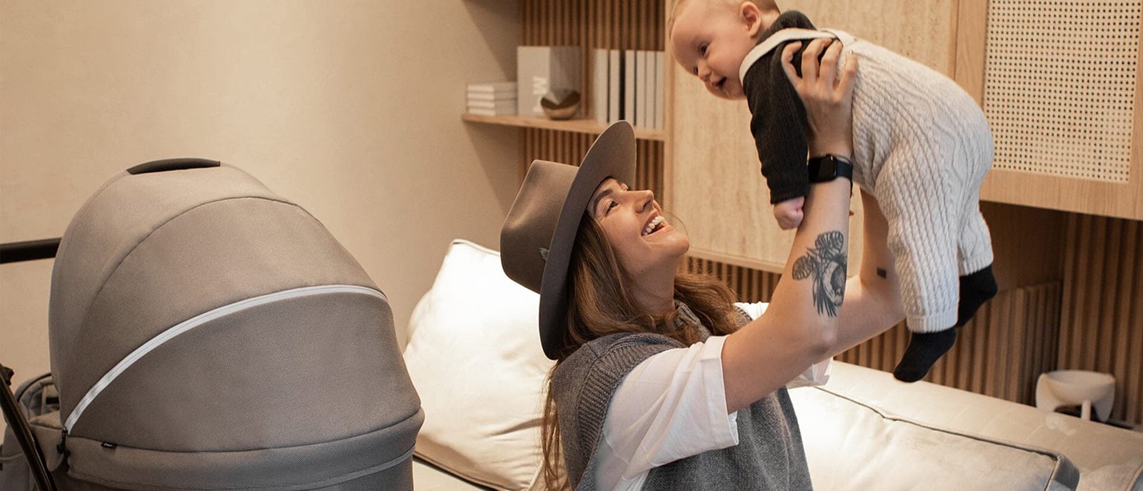 Besijuokianti mama kelia kūdikį šalia Noordi vežimėlio