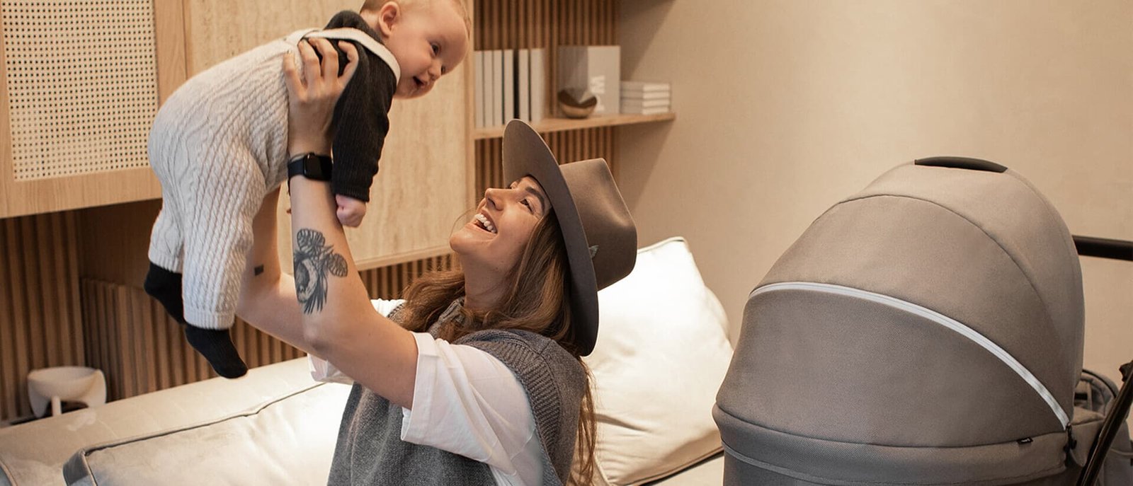 A mother lifting her baby up in a cosy room, a beige carrycot in the foreground