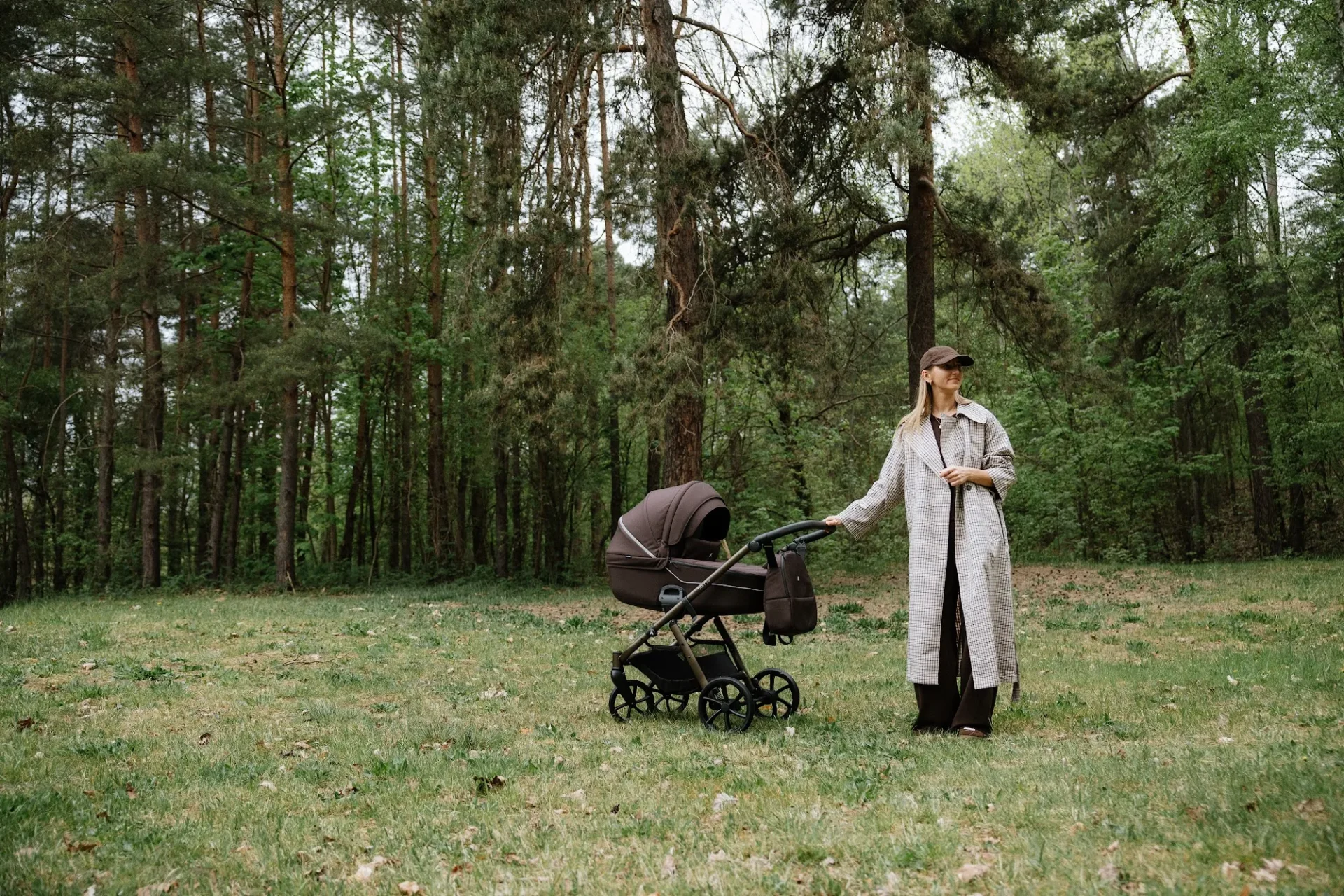 Mother standing beside a Noordi Fjordi V.2 pram at the edge of a pine forest