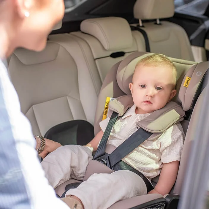 Toddler sitting in a Beno 360 car seat in the back of a car, harness fastened